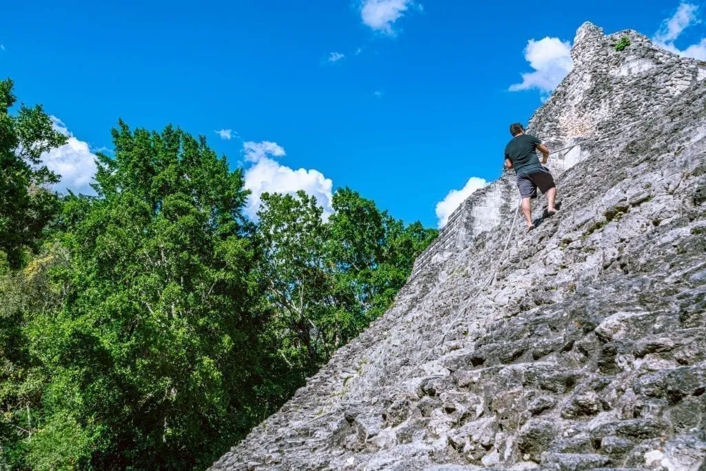 Jeremy Storm climbing a pyramid at the Becan Ruins in Mexico, wearing a black t shirt and pulling on a rope for support