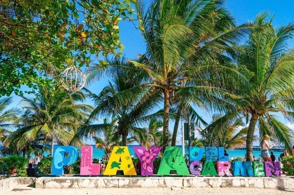 Playa del Carmen colorful sign with palm trees visible in the background