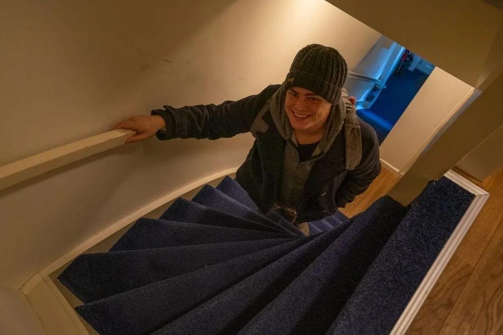 Jeremy Storm wearing a coat and hat climbing a very steep staircase in Amsterdam