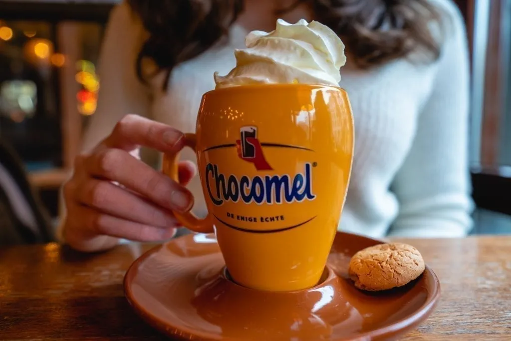 Kate Storm holding out a yellow mug of Chocmel in Amsterdam topped with whipped cream