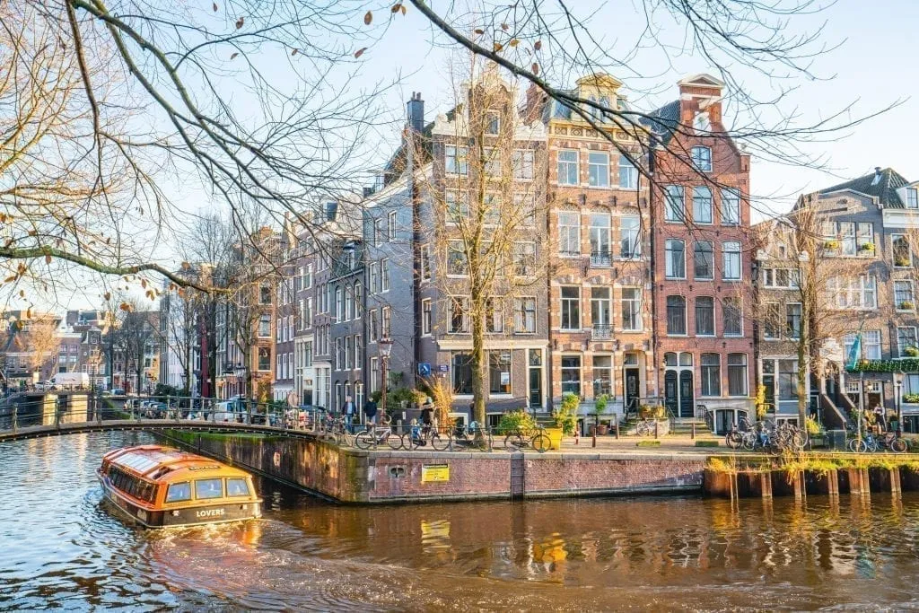 Canal boat floating through Amsterdam as it turns a corner. Typical Dutch houses visible in the background