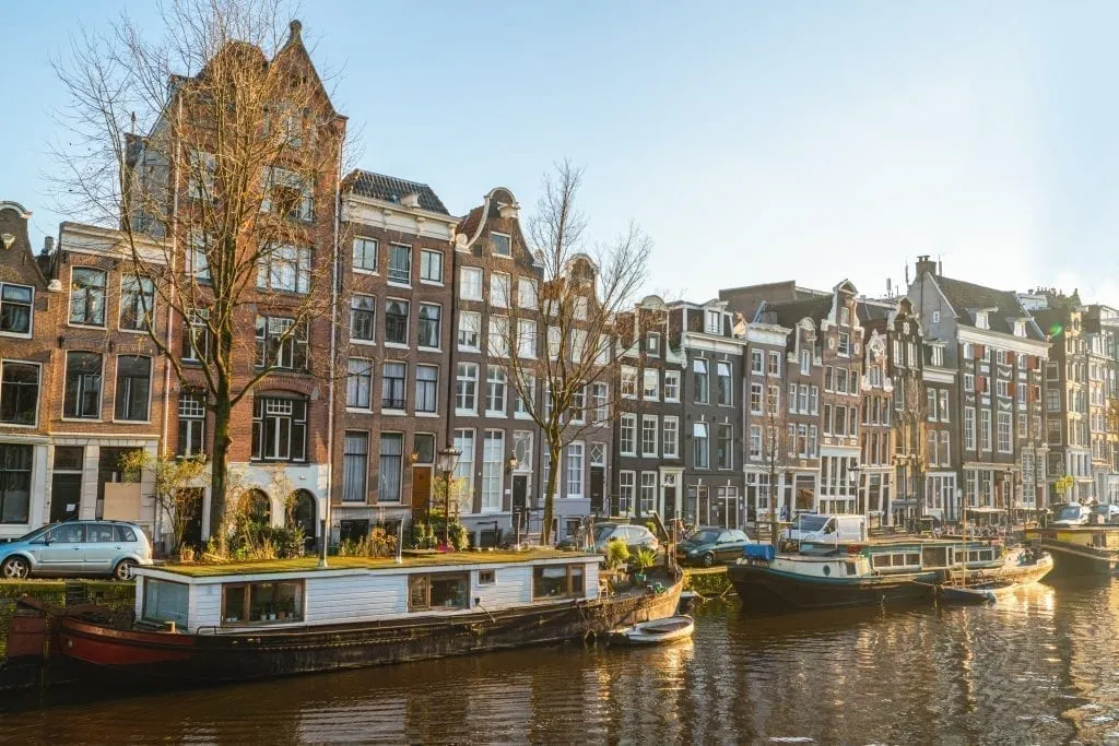 Canal in Amsterdam with houses visible in the background and a hosueboat visible in the foreground