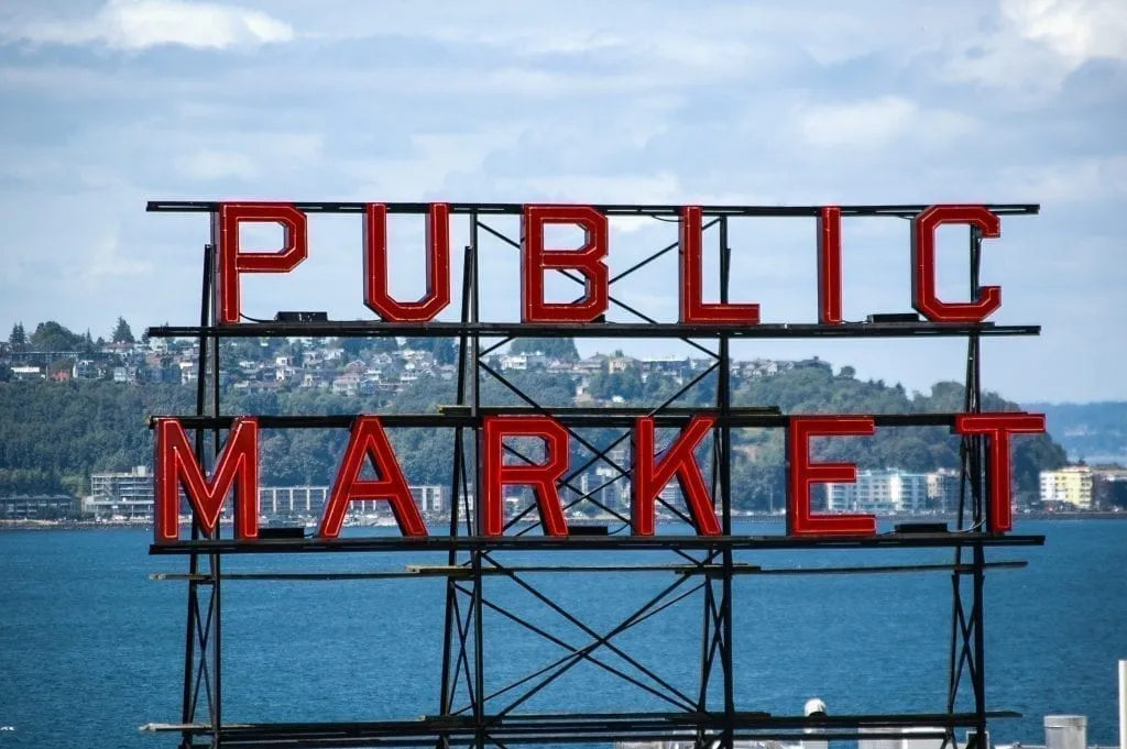 Seattle Public Market red sign with ocean visible in the background. Pike Place Market is an essential stop when stepping 3 days in Seattle Washington!