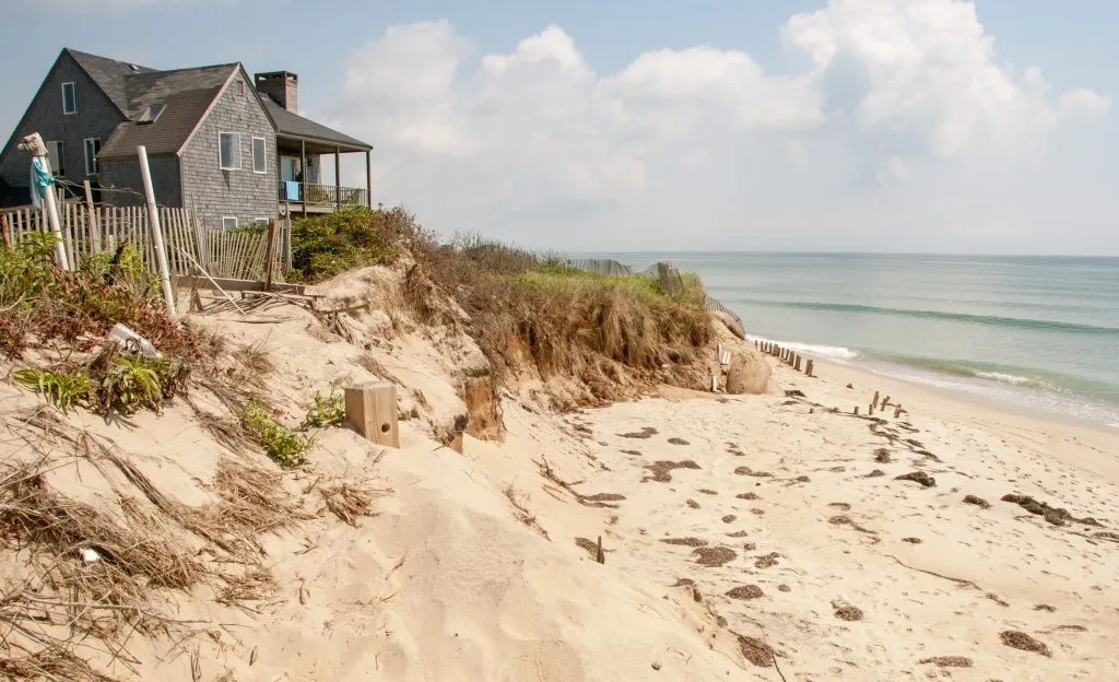 wooden beach house on the coast of marthas vineyard, one of the great honeymoon places in usa, with sand and water to the right of the photo