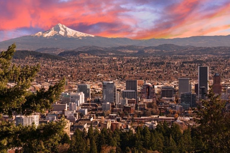 View of Portland skyline with Mt Hood behind it during a pink sunrise, as seen from Pittock Mansion. Be sure to catch the sunshine at least once during your long weekend in Portland itinerary!