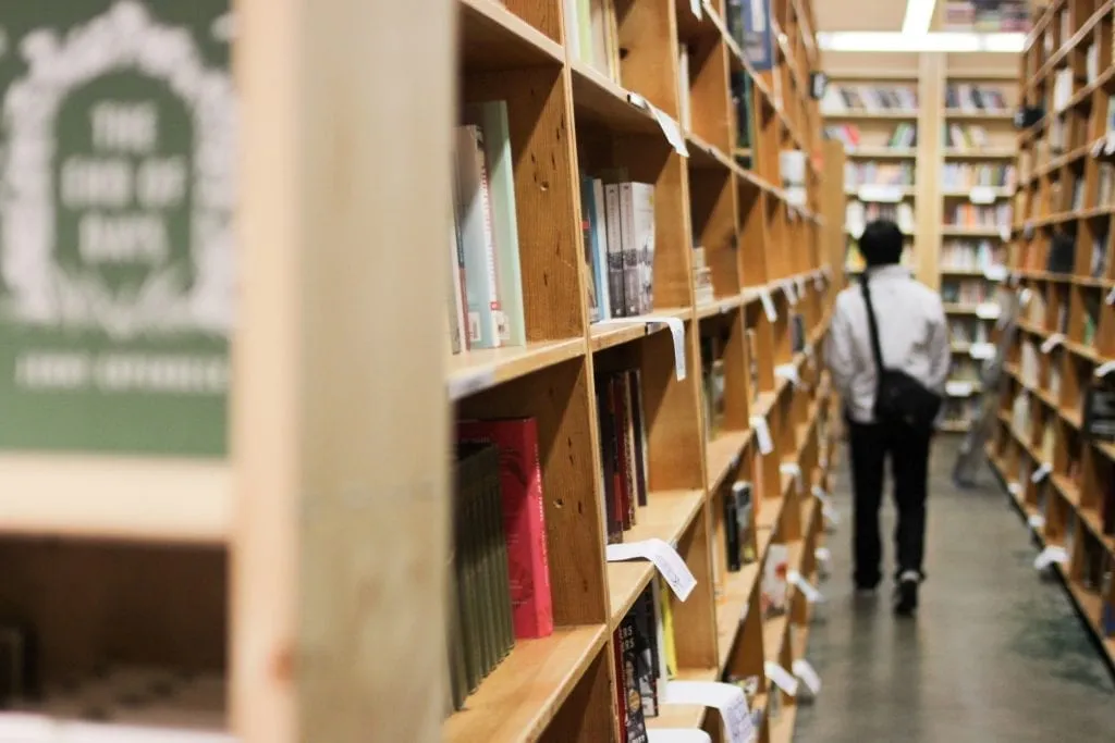 Photo of a man walking away from the camera down an aisle of bookshelves in Powell's City of Books, one of the first stops on this 3 day in Portland weekend getaway itinerary