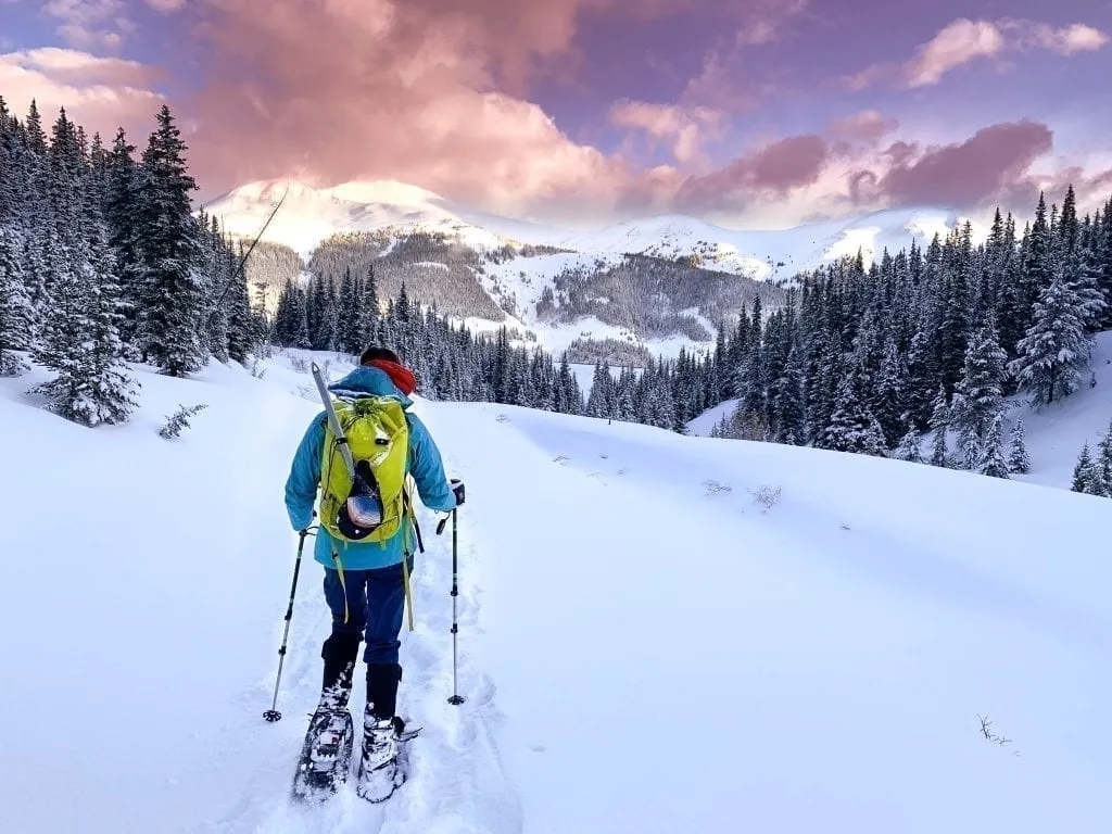 Woman in a blue jacket hiking in the Colorado Rocky Mountains at sunset in winter. The Rocky Mountains are one of the best christmas getaways in the usa