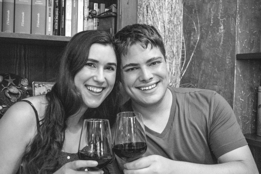 Kate Storm and Jeremy Storm holding up wine glasses in a restaurant in Florence at night. The photo is black and white.