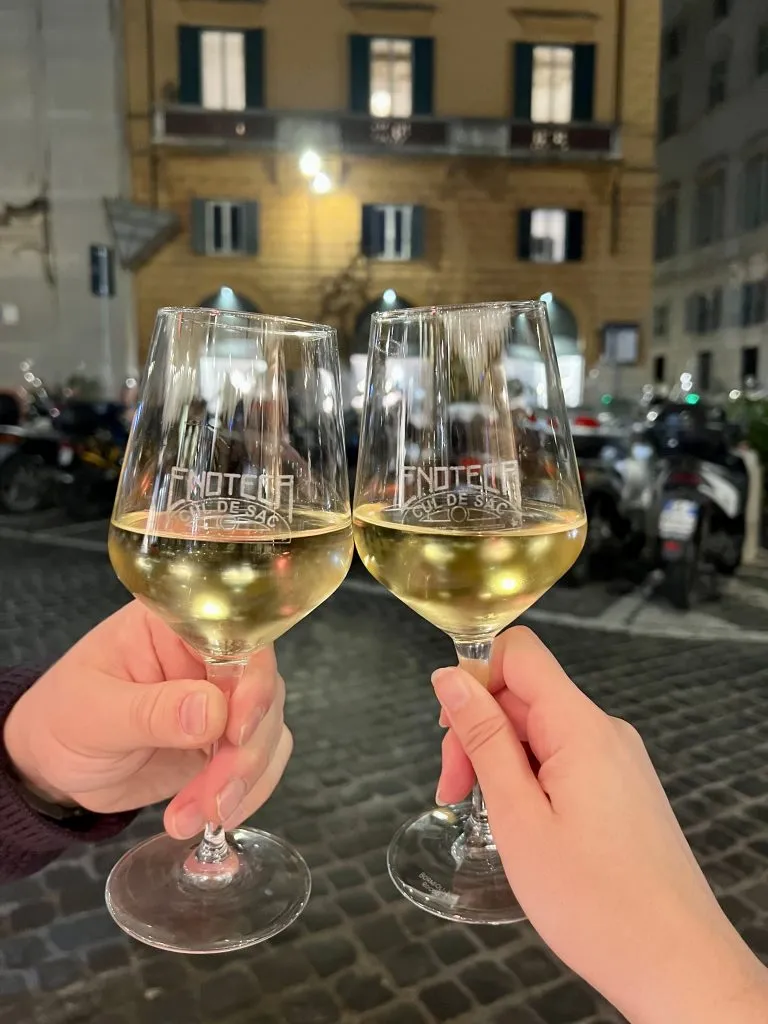 two wine glasses being held out in front of piazza in rome at night