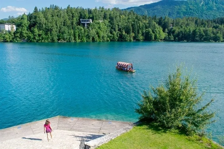 Kate Storm in a pink shirt descending a staircase on Bled Island with the lake visible in the background