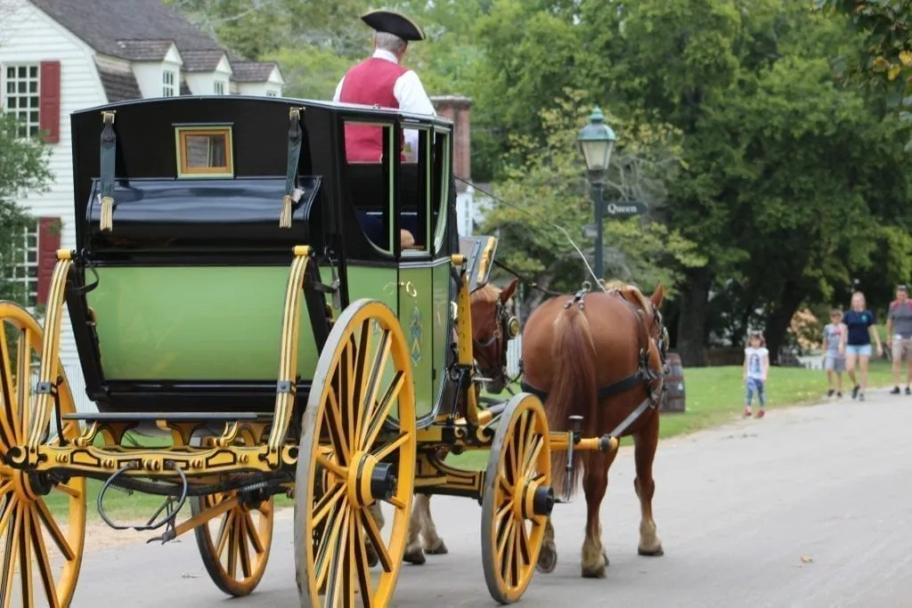 Horse and carriage in colonial Williamsburg that is moving away from the camera on a paved road