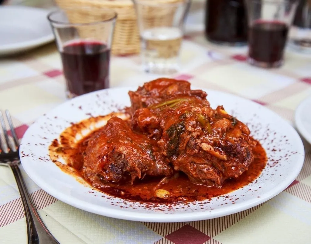 Coda alla vaccinara on a white plate set on a checkered tablecloth--definitely a dish to consider when deciding what to eat in Rome