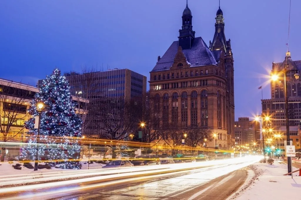 Long exposure of a street scene in Milwaukee at blue hour during the Christmas season, a Christmas tree is visible in the left side of the photo