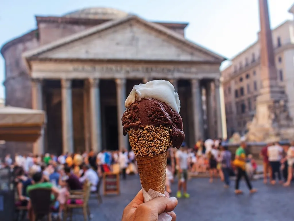 Cone of gelato being held up in front of the Pantheon in Rome. Gelato is definitely a popular food in Rome Italy to consider when deciding what to eat in Rome!