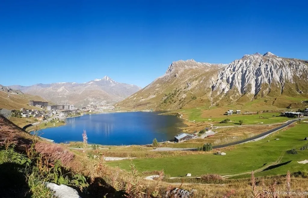 Village of Tignes France in the left of the photo, with most of the image including a mountain lakes and mountains on the right side of the photo. This image is of Tignes in summer.