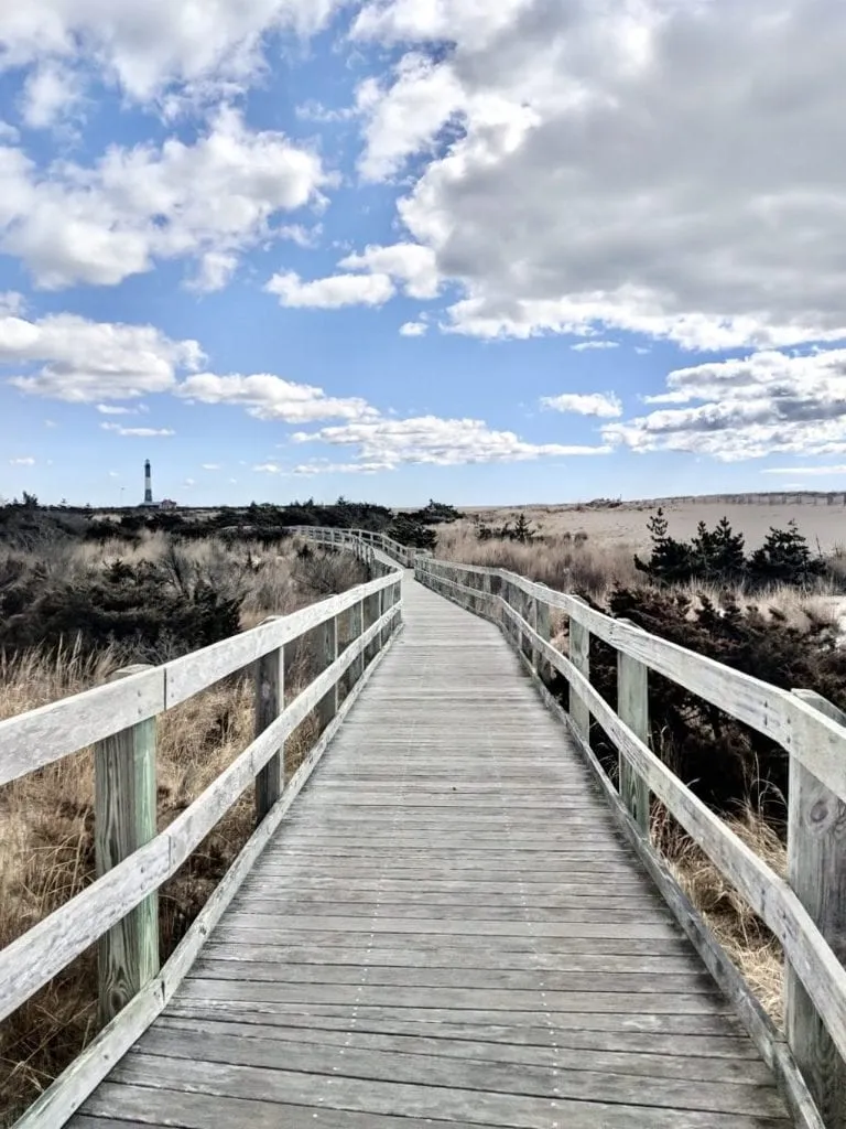 Long stretch of aged wooden boardwalk on Fire Island National Seashore under a partly cloudy sky