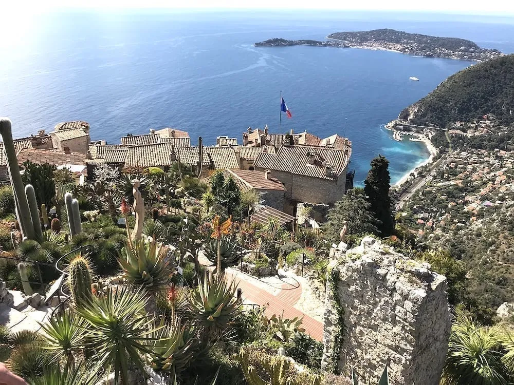 View of Eze from above, with a French flag visible above the village and the Mediterranean Sea in the background. Eze is one of the best small towns in France.