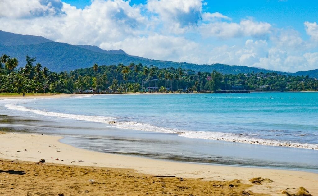Luquillo Beach in Puerto Rica with a blue sky above it and golden sand in the foreground