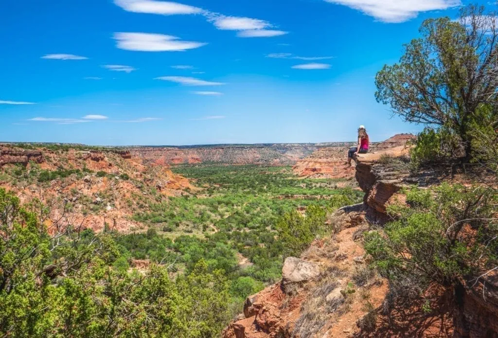 Kate Storm perched on the ledge of Palo Duro Canyon overlooking the green canyon below