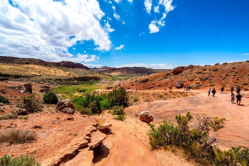 Delicate Arch hike in Arches NP, with a sandstone hill in the foreground and blue sky above