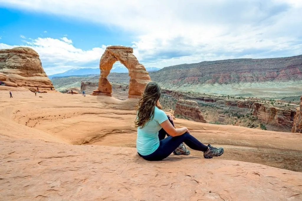Kate Storm in a blue shirt siting in front of Delicate Arch