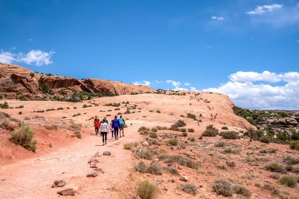 Open sandstone hill in Arches NP with people walking on it