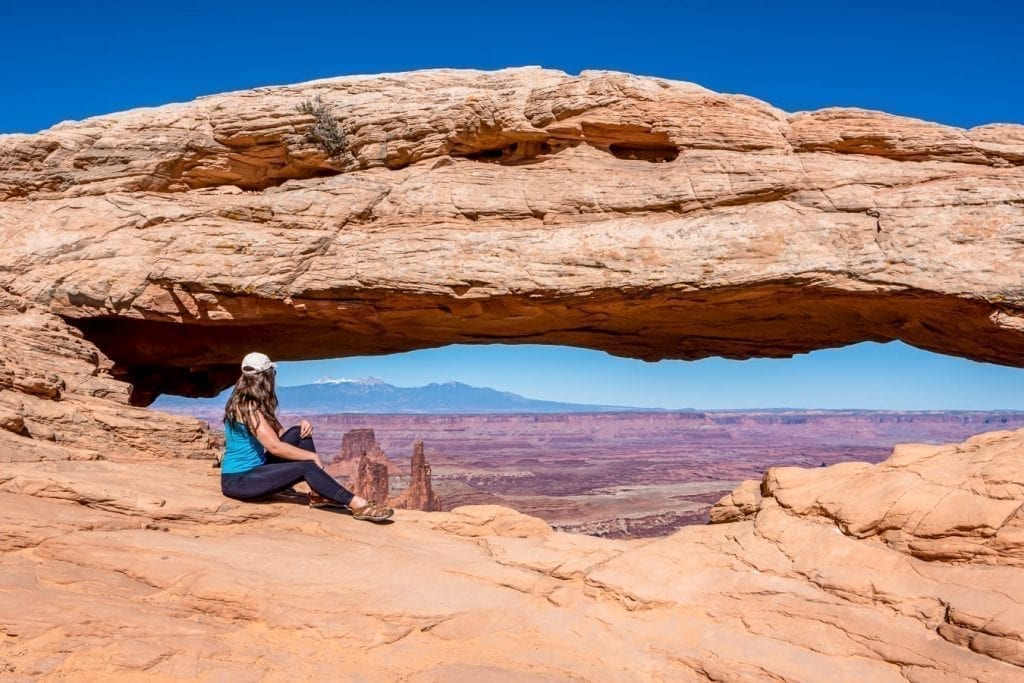 Kate Storm sitting in front of Mesa Arch in Canyonlands National Park, one of the best national parks in usa