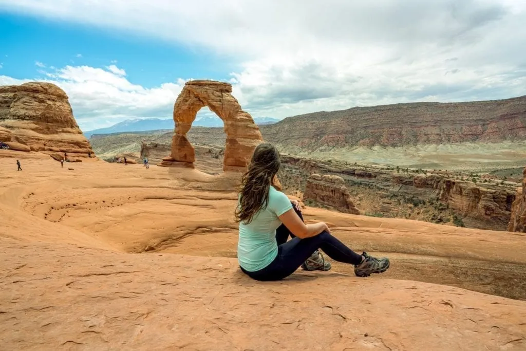 Kate Storm sitting in front of Delicate Arch Utah wearing a turquoise shirt