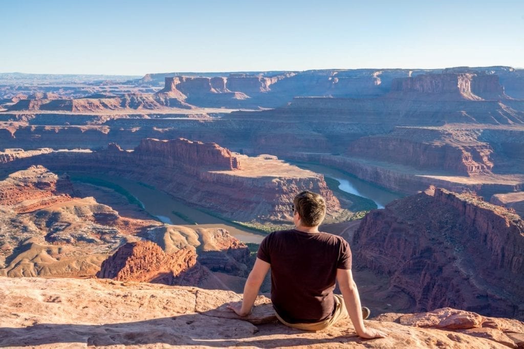 Jeremy Storm sitting on a ledge overlooking Dead Horse Point State Park near sunset as part of a Utah national parks road trip