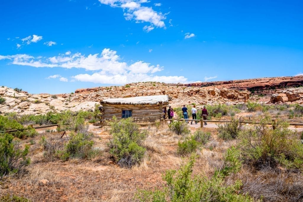 Wolfe Ranch Cabin on the Delicate Arch hike in Arches NP with a blue sky. Desert is in the foreground in front of the cabin