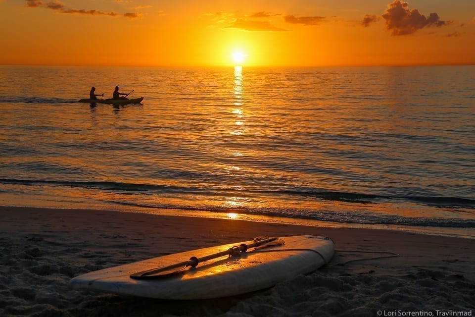 Beach in Naples Florida at sunset, with a paddleboard in the foreground and a bright orange sunset over the water
