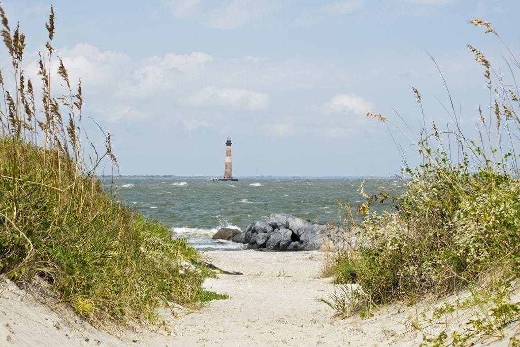 Sandy pathway to Folly Beach near Charleston South Carolina with the Morris Lighthouse visible in the water in the distance