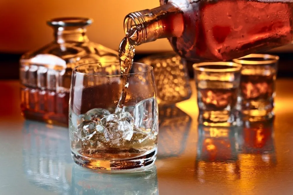 Glass of whiskey being poured into a highball glass holding ice cubes. Whiskey is one of the best things to buy in Ireland