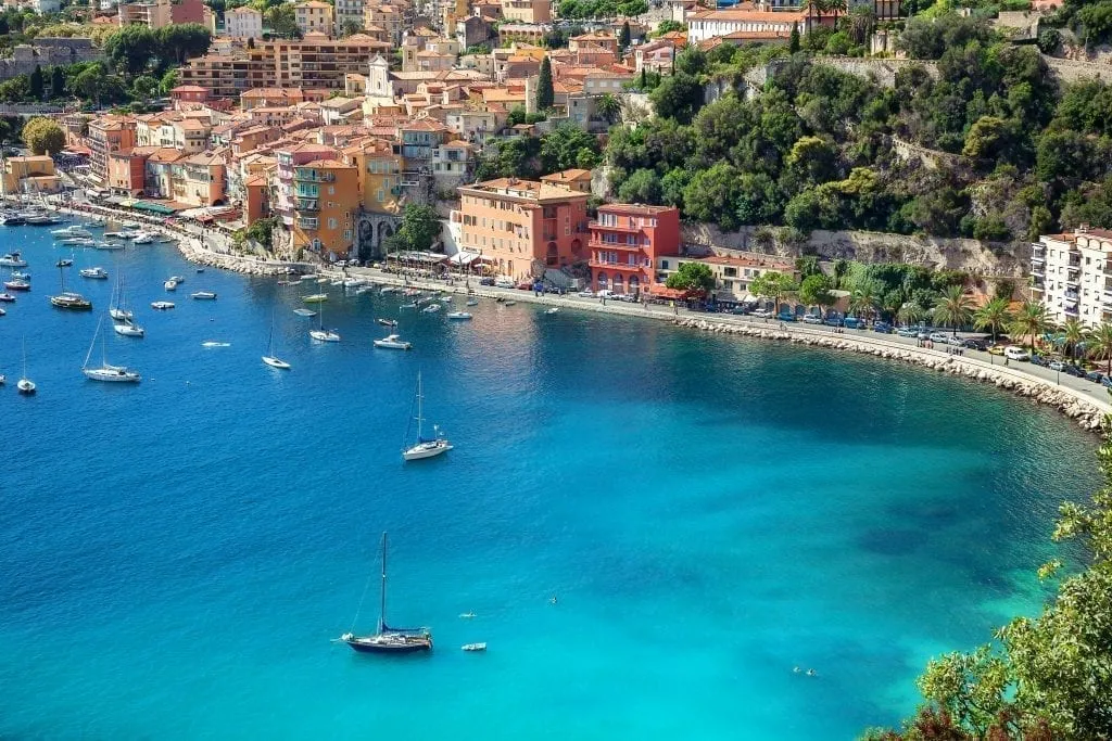 Villefranche-sur-Mer as seen from across the water with sailboats and water in the foreground. Villefranche-sur-Mer is one of the prettiest villages in France