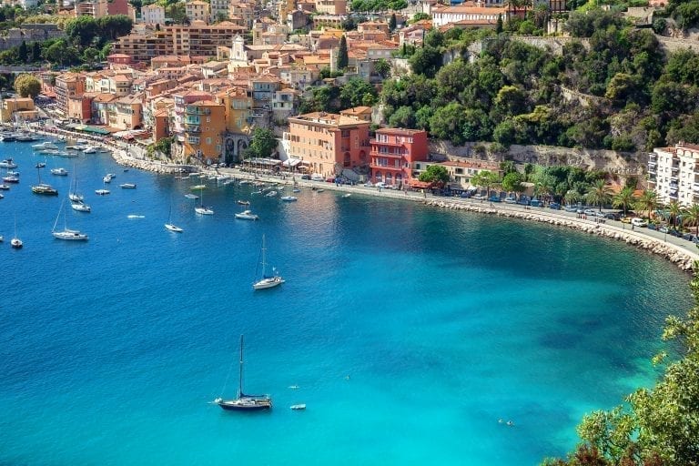 Villefranche-sur-Mer as seen from across the water with sailboats and water in the foreground. Villefranche-sur-Mer is one of the prettiest villages in France