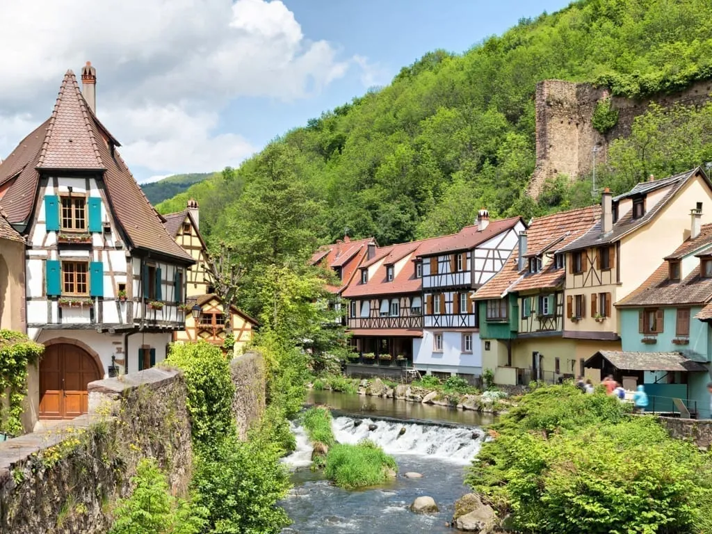 Kaysersberg France in Alsace with colorful buildings on either side of a flowing river. Kaysersberg is one of the prettiest small towns in France