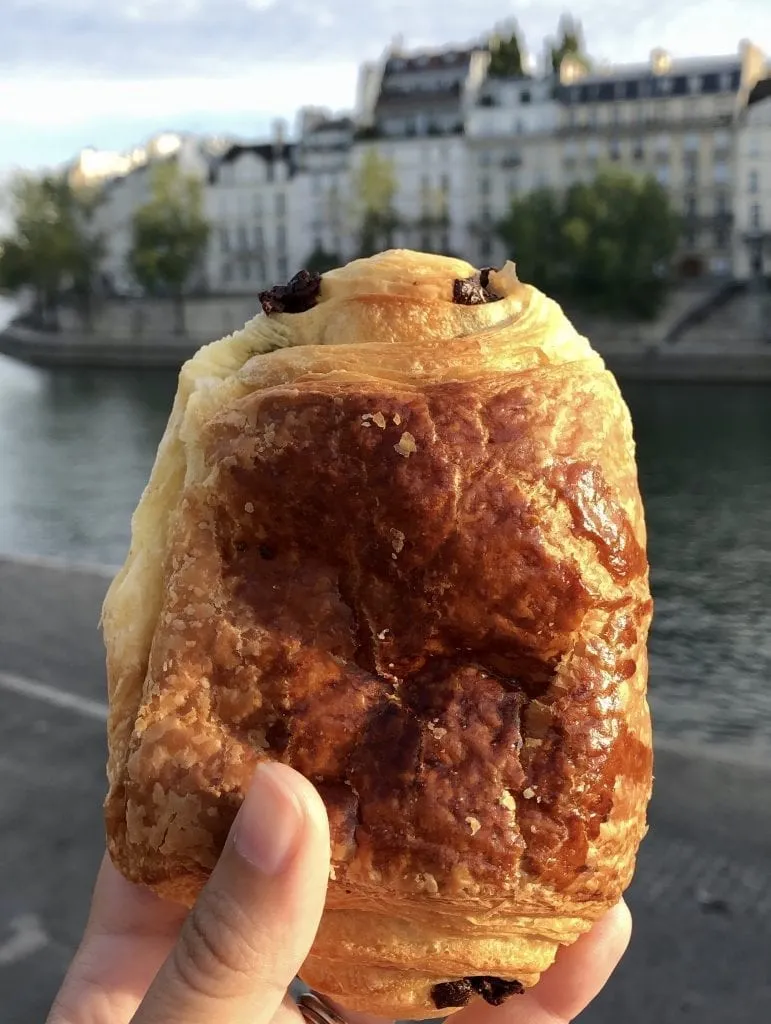 Pain au chocolat being held up in front of the Seine in Paris. Pain au chocolats are one of the most popular French breakfast foods