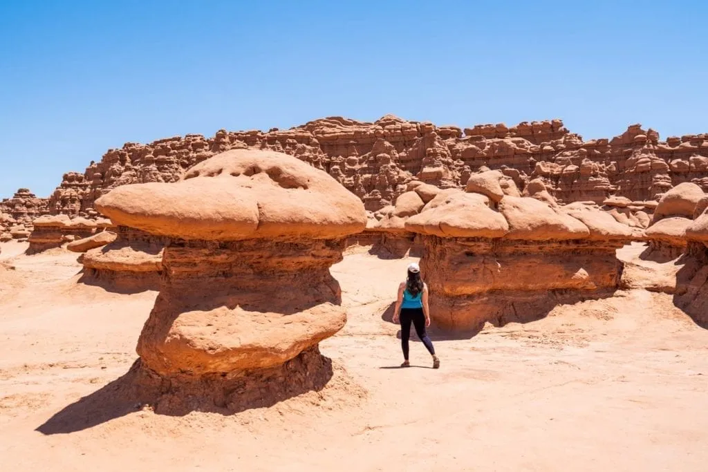 Kate Storm wearing a blue tank top walking between two formations in Goblin Valley State Park Utah