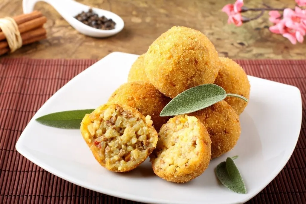 Plate of 6 arancini balls with one cut in half. Arancini are a typical Sicilian street food