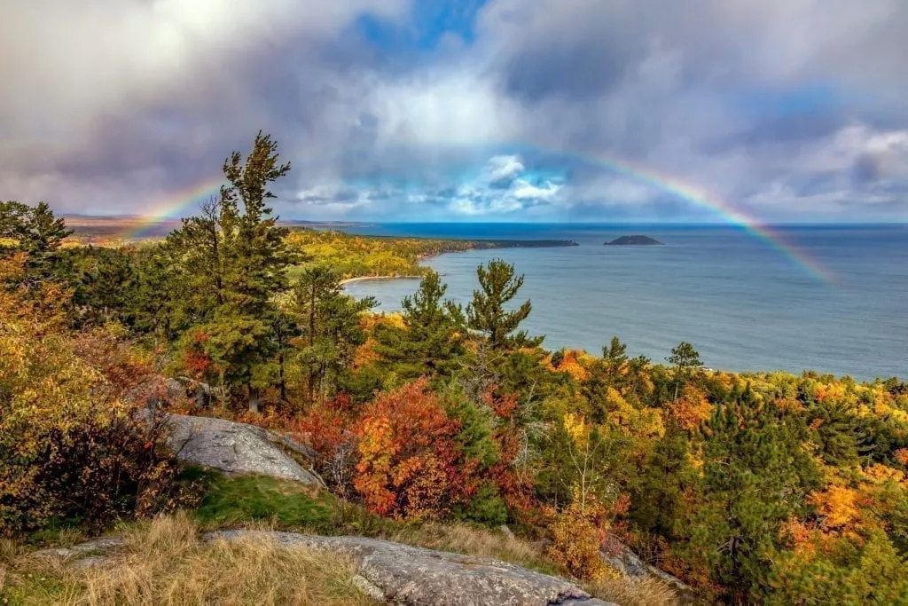 View of Lake Superior with a rainbow over it during fall foliage season on Sugarloaf Mountain in Michigan