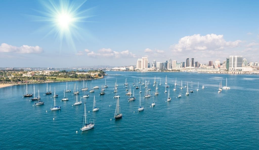 San Diego CA harbor with rows of sailboats in the foreground and the skyline in the back right of the photo