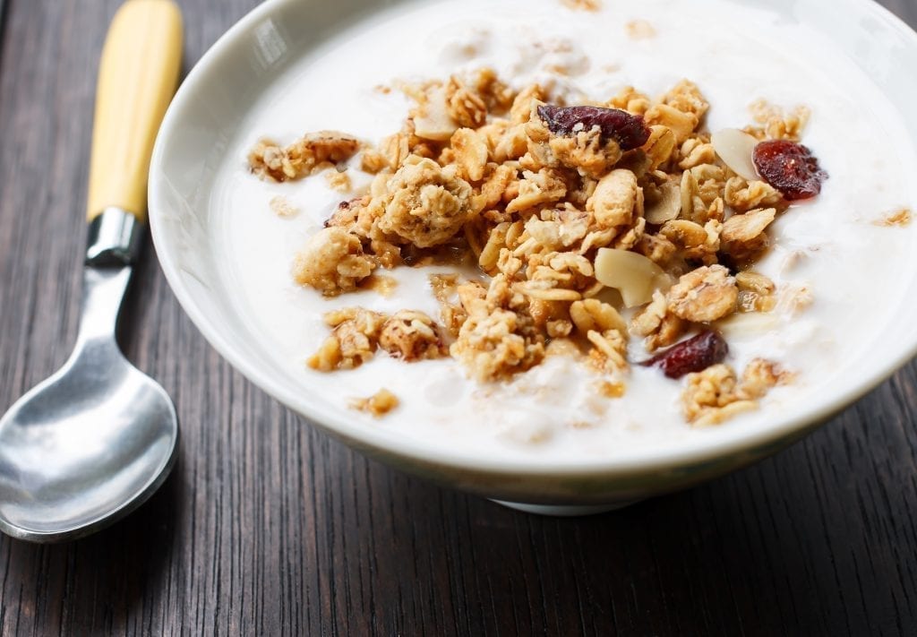 Bowl of yogurt with muesli on top on a white bowl with a spoon to the left of the bowl.