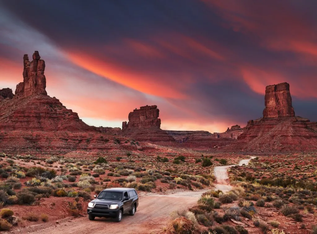 black suv driving through dirt road in valley of the gods utah at sunset