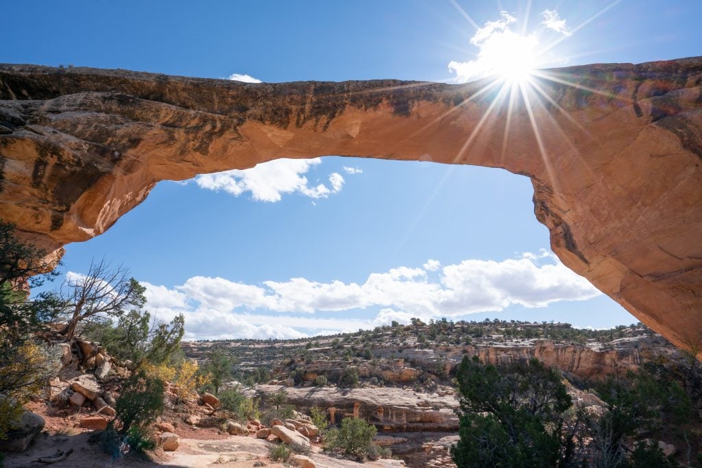 Owachomo bridge in natural bridges state park with a sun flare behind it, one of the best utah vacation spots