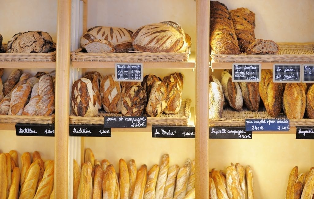 Shelf of a boulangerie in France displaying various breads on wooden shelves