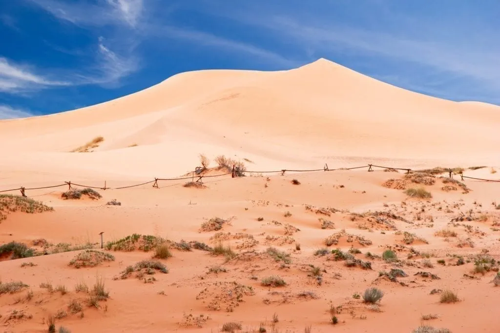 Coral Pink Sand Dunes State Park in Utah on a sunny day with a large dune in the center of the frame. This park is one of the best places to visit in Utah