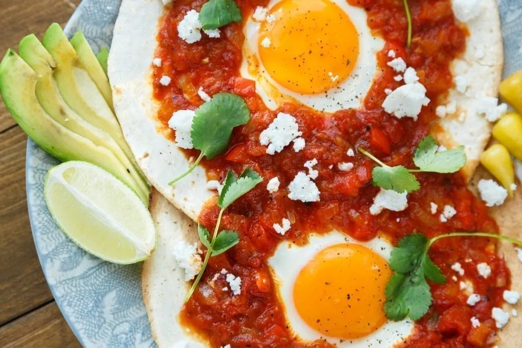 2 huevos rancheros as seen from above with red sauce on top and avocado to the left side