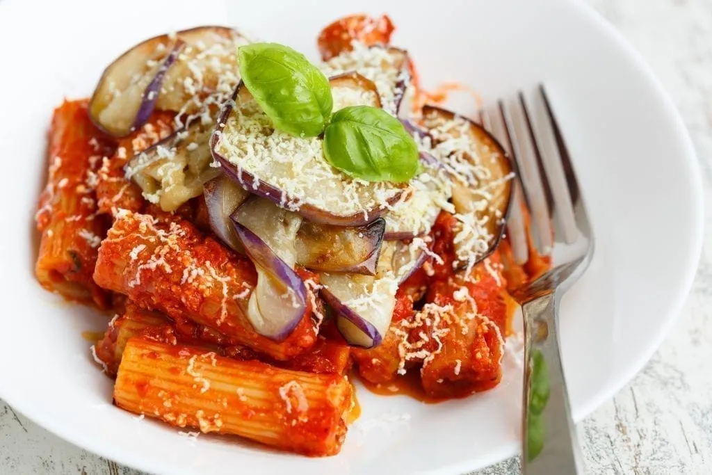 Pasta alla Norma topped with eggplant in a white bowl with a silver fork next to it