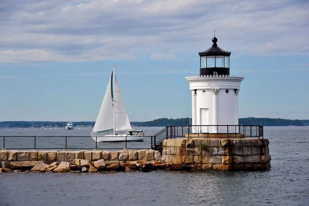 Portland Bug Light as seen from the side with a sailboat passing by behind it