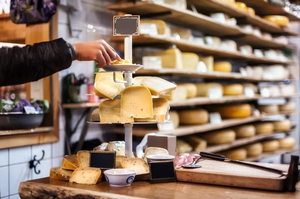 Tray of cheeses for sale in Amsterdam with a shelf full of cheese wheels visible in the background